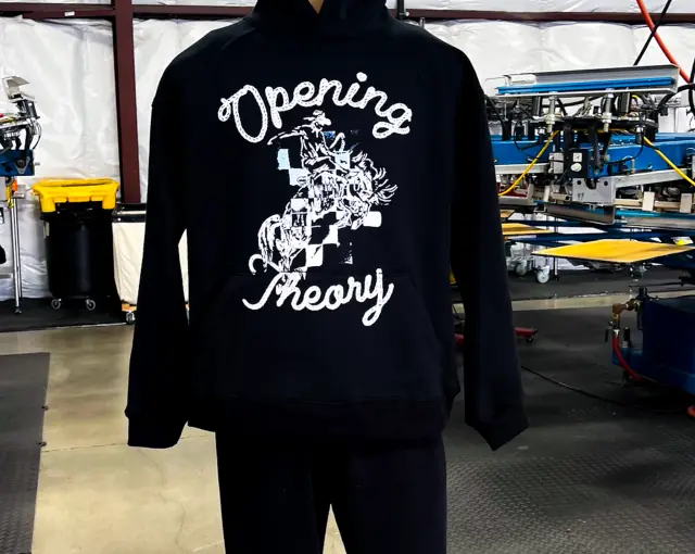 Black hoodie on a form with a white rope-script and bronco rider print running over the kangaroo pocket, presses behind