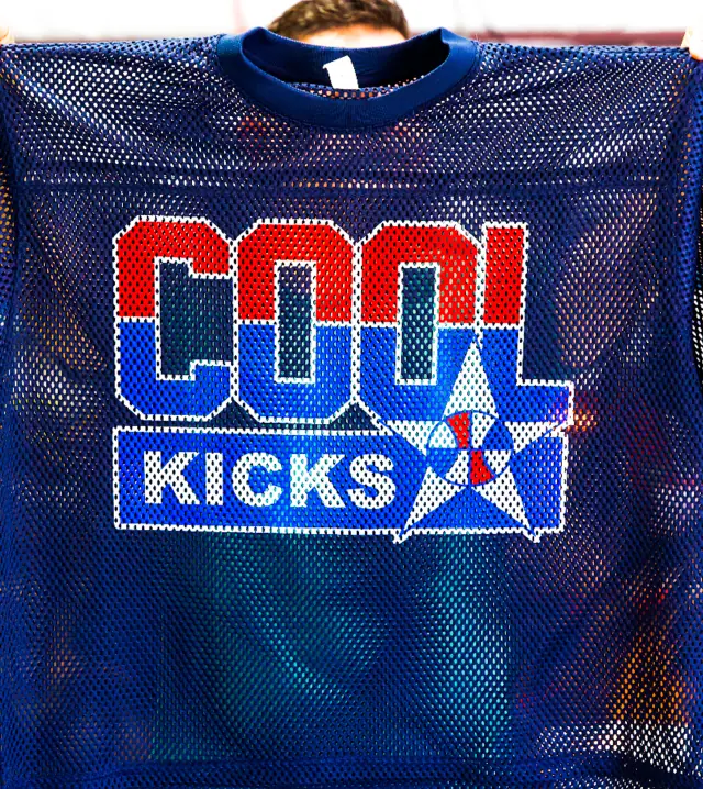 Person holds up a navy mesh jersey with a red, white and blue block lettering and star logo print on the front