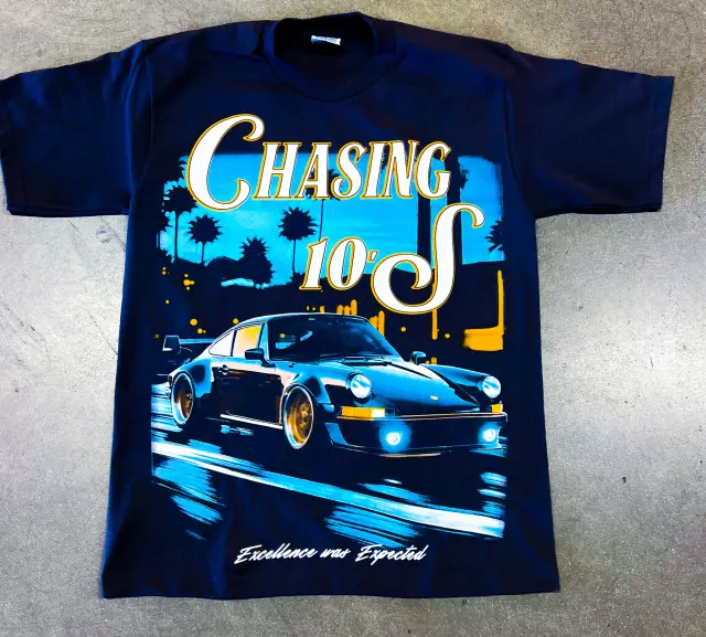 Navy tee laid on concrete with a large multi-color print of a sports car at night under palm trees and script text