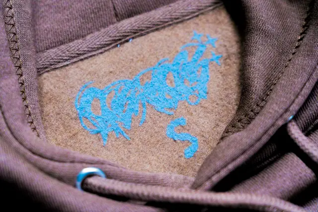 Close-up inside the neck of a mauve hoodie showing a light blue printed tagless logo and size S on the fleece lining