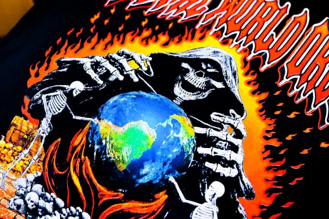 Close-up of a detailed multi-color print of a hooded skeleton holding a globe in flames, showing layered ink on black fabric