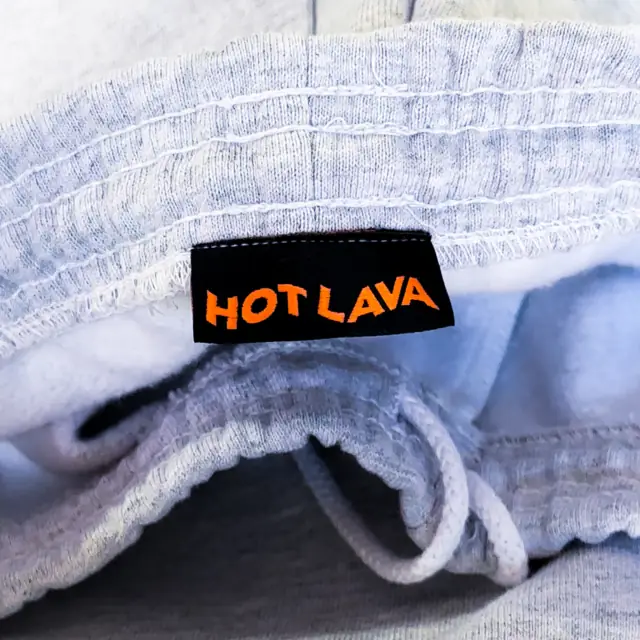 Black woven label with orange lettering sewn inside the waistband of heather gray fleece bottoms with a white drawstring